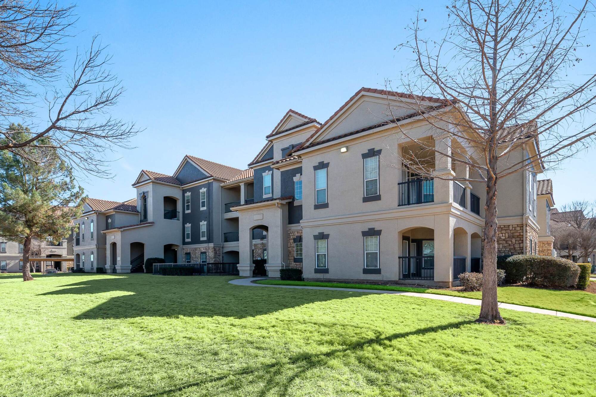 Modern apartment buildings with balconies and large windows facing a sunny lawn at Belterra in Fort Worth, Texas