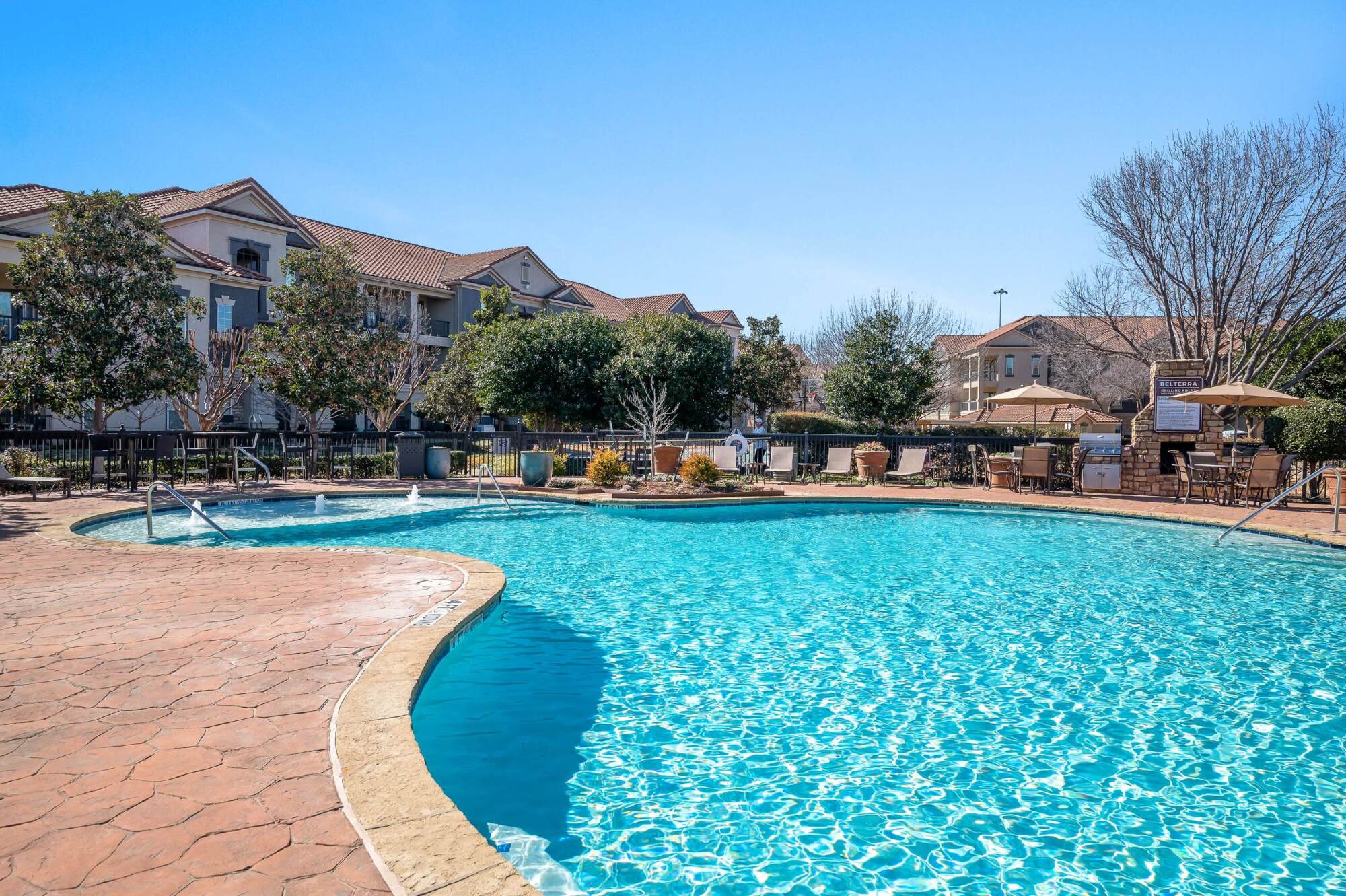 Outdoor swimming pool surrounded by lounge chairs and shade trees at Belterra apartments in Fort Worth, Texas